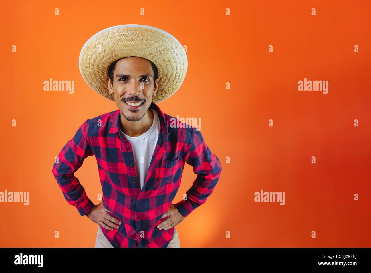 Black Man con Junina Party vestito isolato su sfondo arancione. Giovane uomo che indossa abiti tradizionali per Festa Junina - Festival brasiliano di giugno. Foto Stock