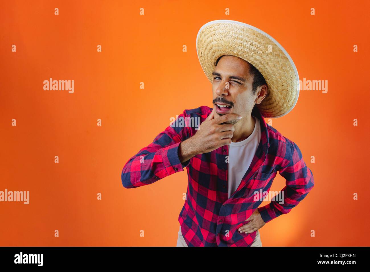 Black Man con Junina Party vestito isolato su sfondo arancione. Giovane uomo che indossa abiti tradizionali per Festa Junina - Festival brasiliano di giugno. Foto Stock