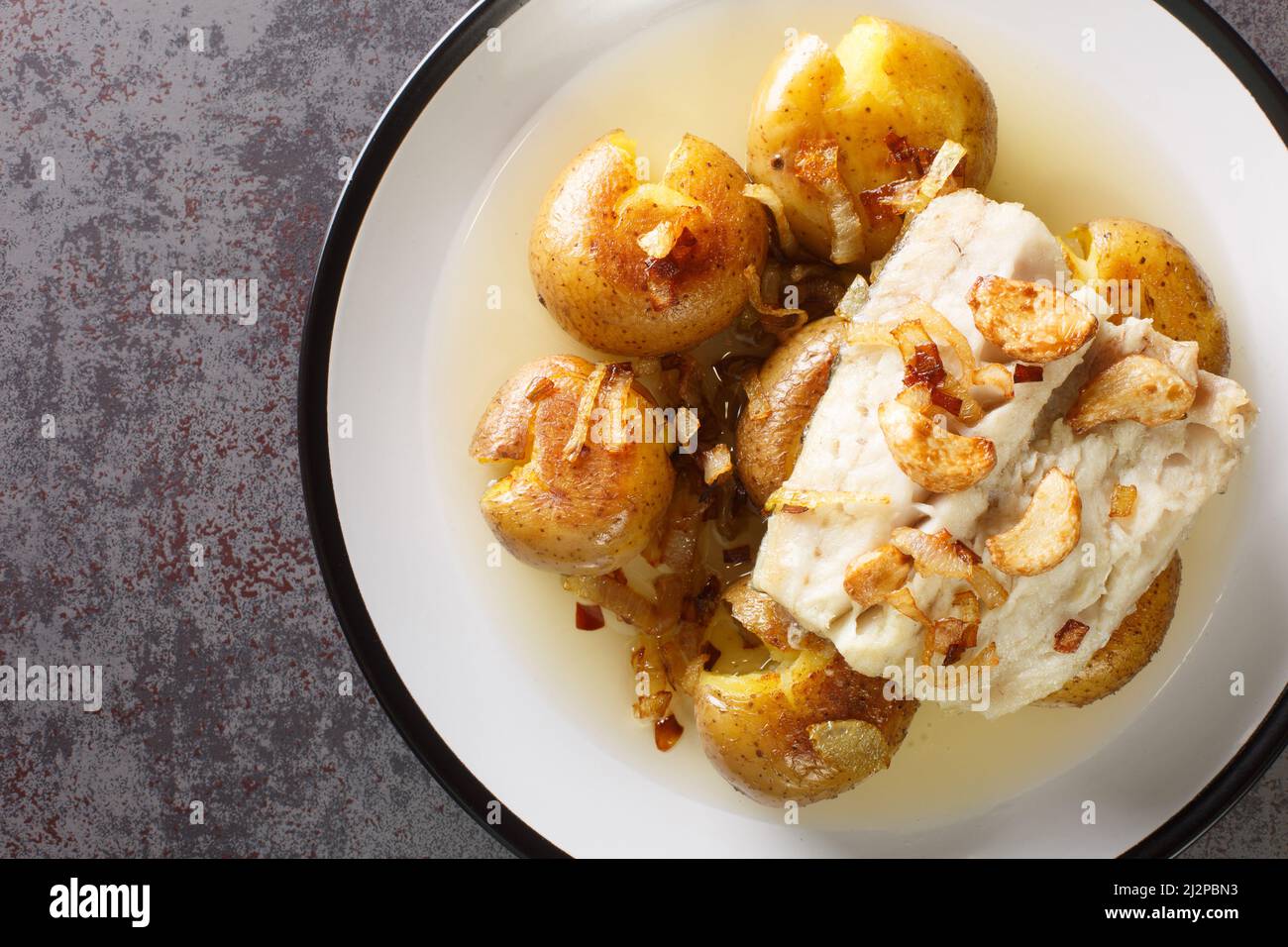 Portoghese Bacalhau a Lagareiro merluzzo salato cotto in olio con patate primo piano in un piatto sul tavolo. Vista dall'alto orizzontale dall'alto Foto Stock