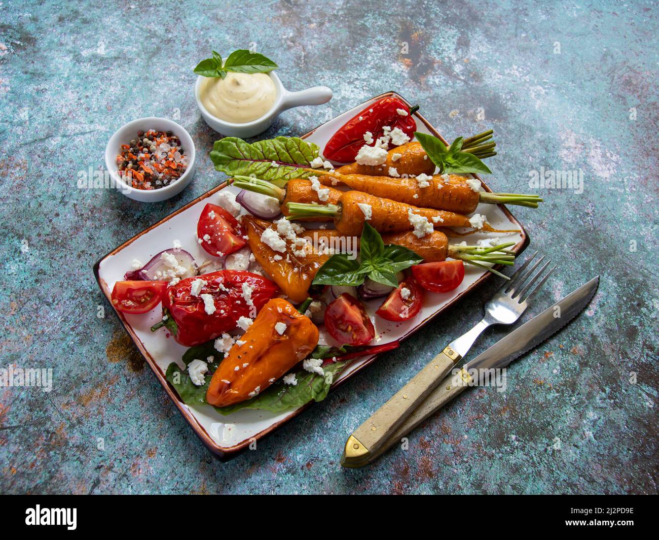 carote al forno, pomodoro, peperone in un piatto, basilico e spezie piatto vegano, primo piano, salsa gialla Foto Stock