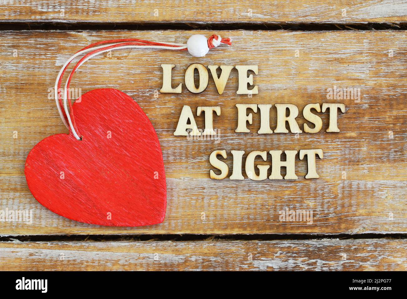 Amore a prima vista scritto con lettere di legno su superficie rustica e cuore di legno rosso Foto Stock