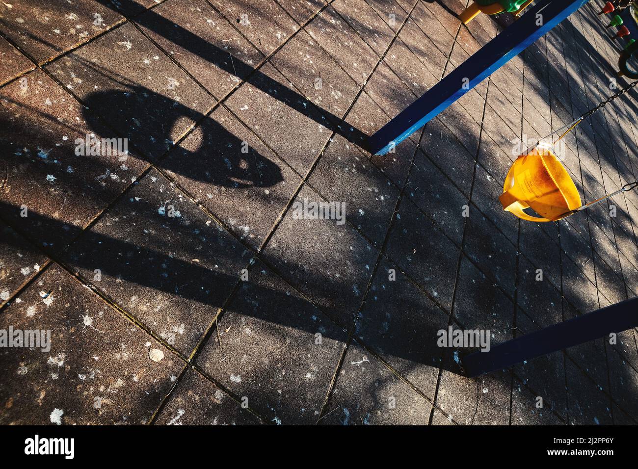 Un'altalena per bambini nel parco con una forte ombra sul pavimento. Foto Stock