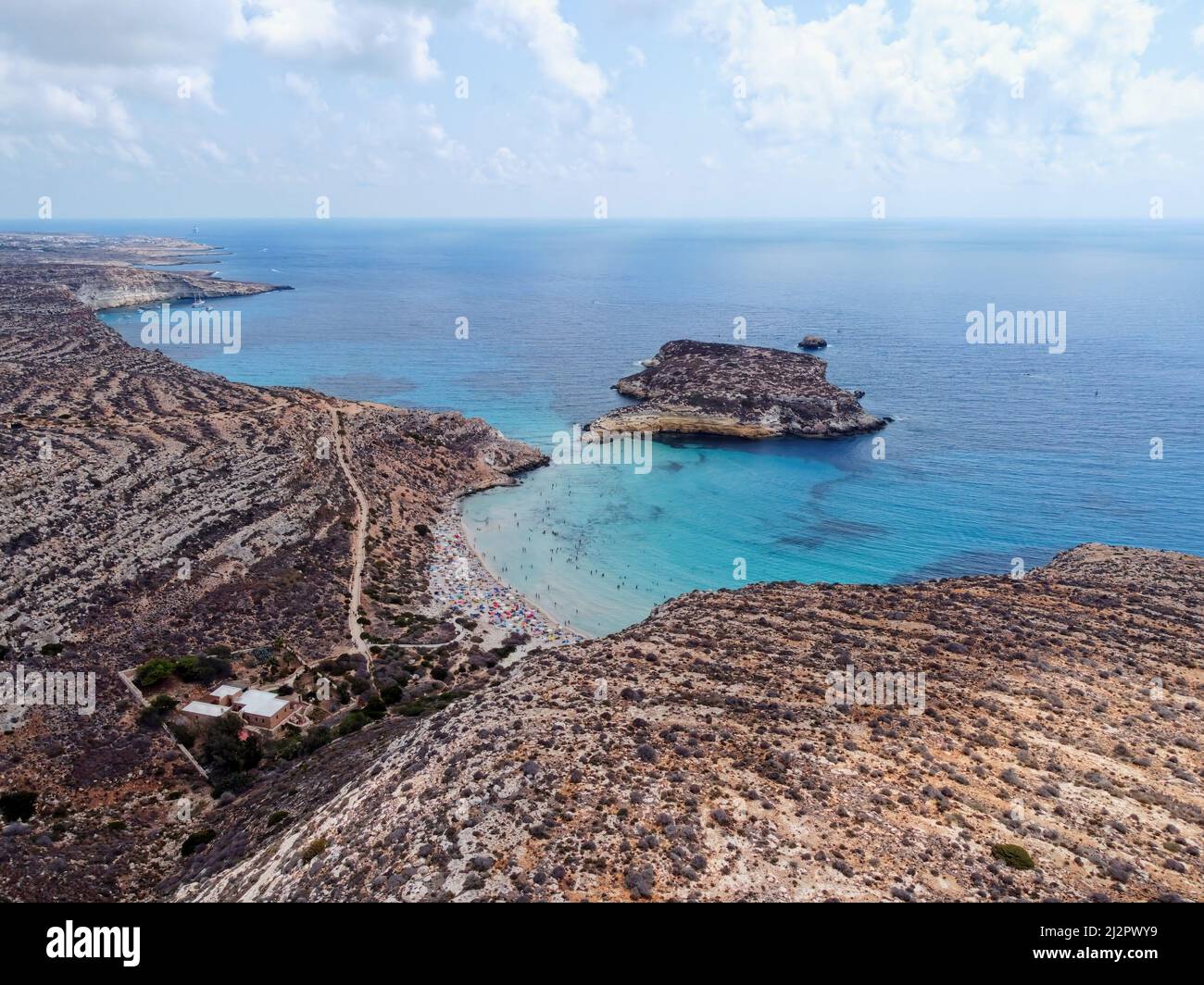 Drone aereo. Spiaggia e Isola dei Conigli, Lampedusa. Tranquilla spiaggia in stile baia con sabbia bianca e surf turchese delimitato da scogliere rocciose. Foto Stock