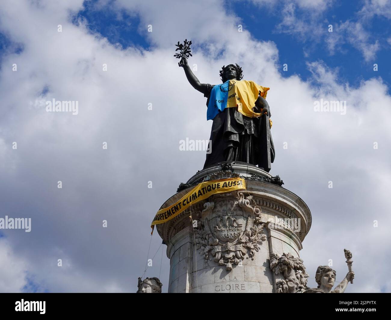 Monumento alla Repubblica, adornato con un gilet giallo e blu nei colori della bandiera Ucraina, insieme con il simbolo della ribellione di estinzione, movimento internazionale sociale ambientale, in protesta della guerra in Ucraina e l'uso eccessivo di petrolio e il suo ruolo nella distruzione del clima. 2 aprile 2022, Parigi, Francia Foto Stock