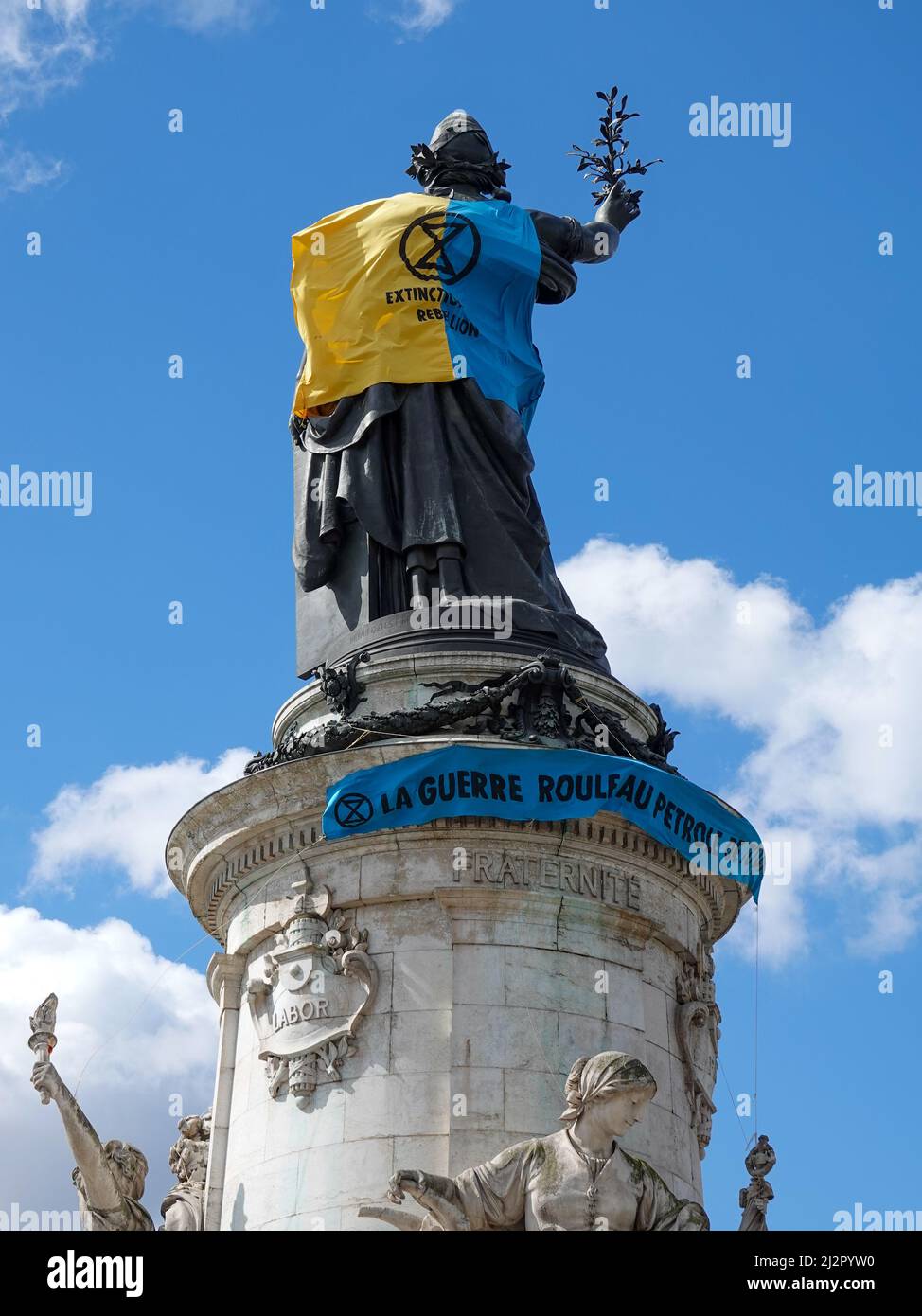 Monumento alla Repubblica, adornato con un gilet giallo e blu nei colori della bandiera Ucraina, insieme con il simbolo della ribellione di estinzione, movimento internazionale sociale ambientale, in protesta della guerra in Ucraina e l'uso eccessivo di petrolio e il suo ruolo nella distruzione del clima. 2 aprile 2022, Parigi, Francia Foto Stock