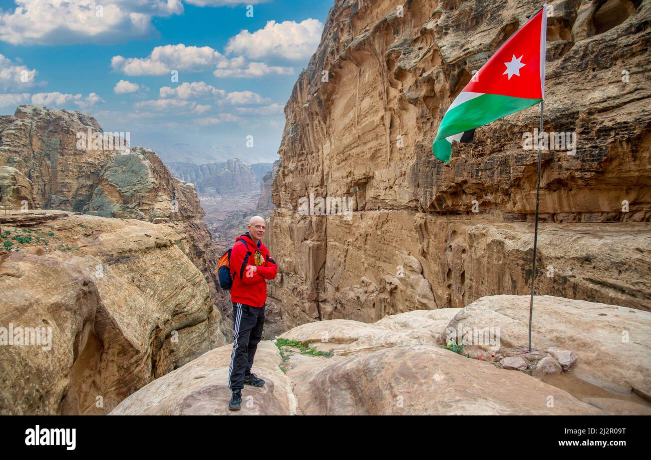 Un turista si pone accanto alla bandiera giordana che vola a Petra con belle montagne rosse sullo sfondo e cielo blu 20 febbraio 2020 Foto Stock