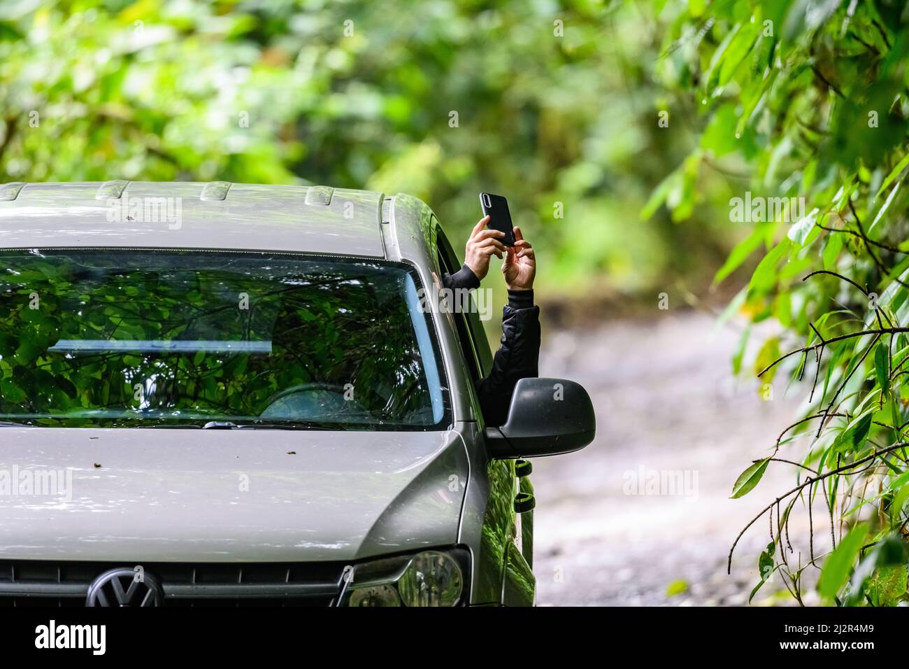 Un uomo che prende un'immagine del telefono delle cellule dalla sua finestra dell'automobile. Colombia, Sud America. Foto Stock