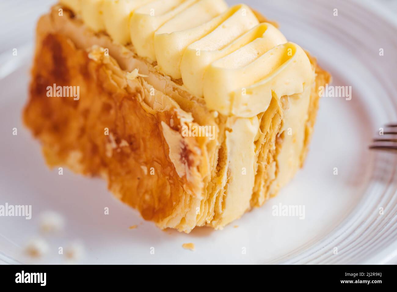 Dessert francese chiamato Mille Feuille o torta Napoleone decorato con fiori in fiore su sfondo luminoso. Torta gustosa a strati con crema alla vaniglia e pu Foto Stock