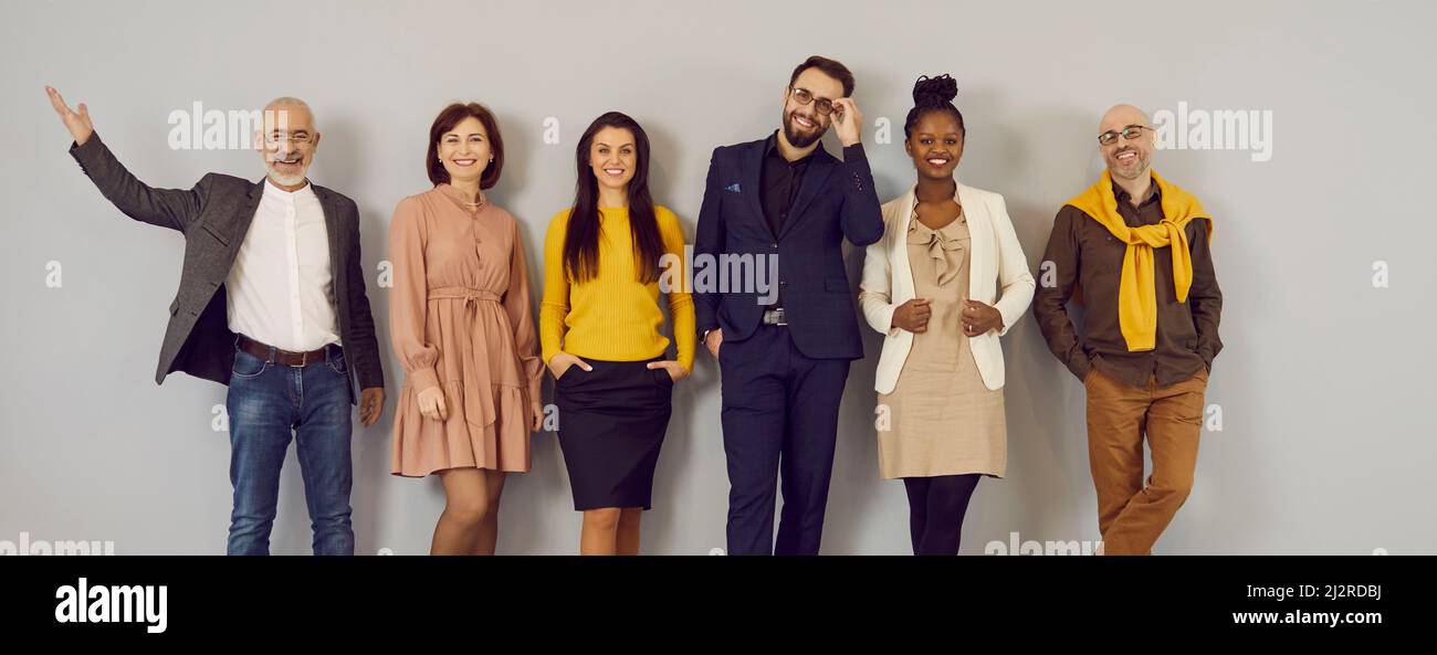 Un gruppo vario di persone felici in abiti casual elegante che si posa contro la parete dello studio Foto Stock