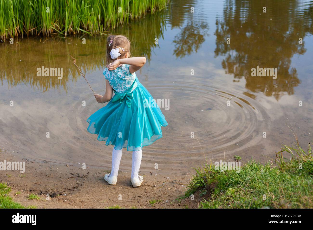 Una ragazza in un abito blu getta ciottoli in acqua. Un bambino gioca con il fiume in natura. Un bambino elegantemente vestito sta divertendosi vicino al lago. CHIL Foto Stock