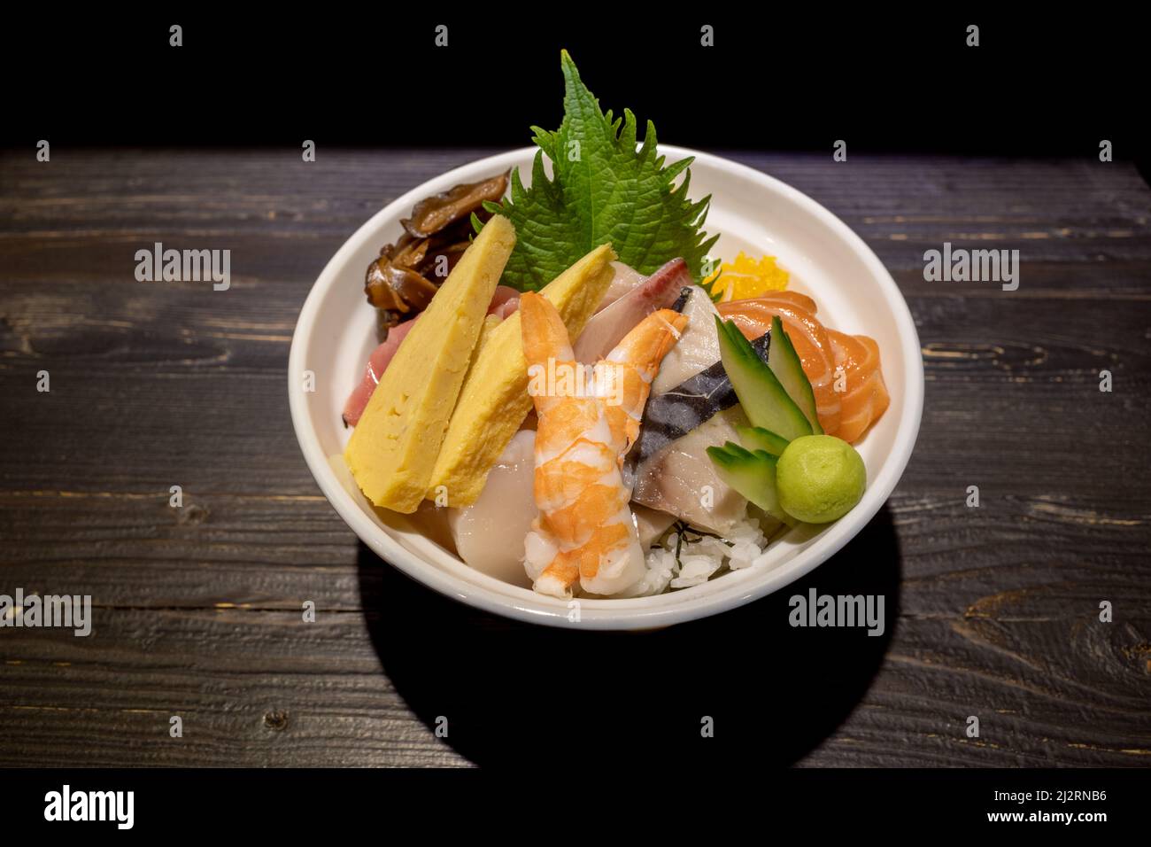 Vista dall'alto di Sashimi Don, Danburi o ciotola di riso giapponese con varie fette di pesce fresco, gamberi, calamari e uova di tamago, sul banco scuro in legno. Foto Stock