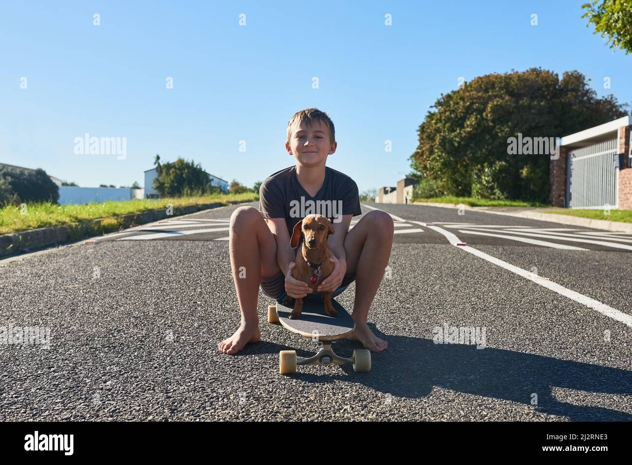 Insegnare il mio cane deve pattinare. Ritratto a tutta lunghezza di un ragazzo e del suo cane seduto su una tavola lunga. Foto Stock