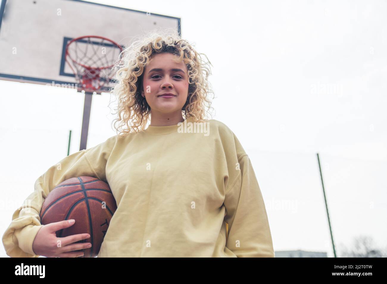 Bella giovane donna bionda tiene una palla di basket sul campo, sorridendo alla fotocamera medio scatto copia spazio . Foto di alta qualità Foto Stock