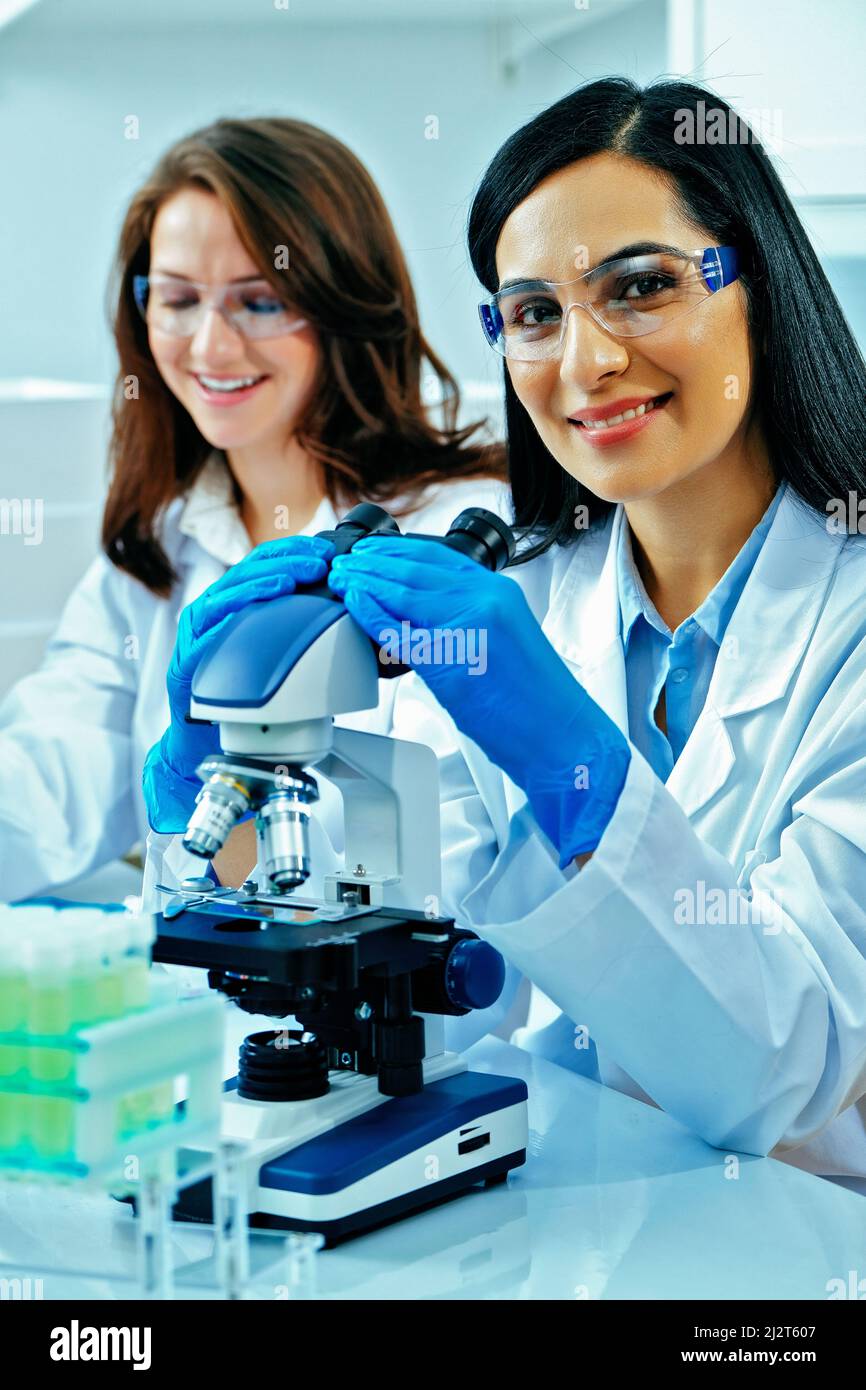 Giovane scienziata femminile che usa il microscopio mentre la sua collega che lavora nell'industria farmaceutica di base Foto Stock