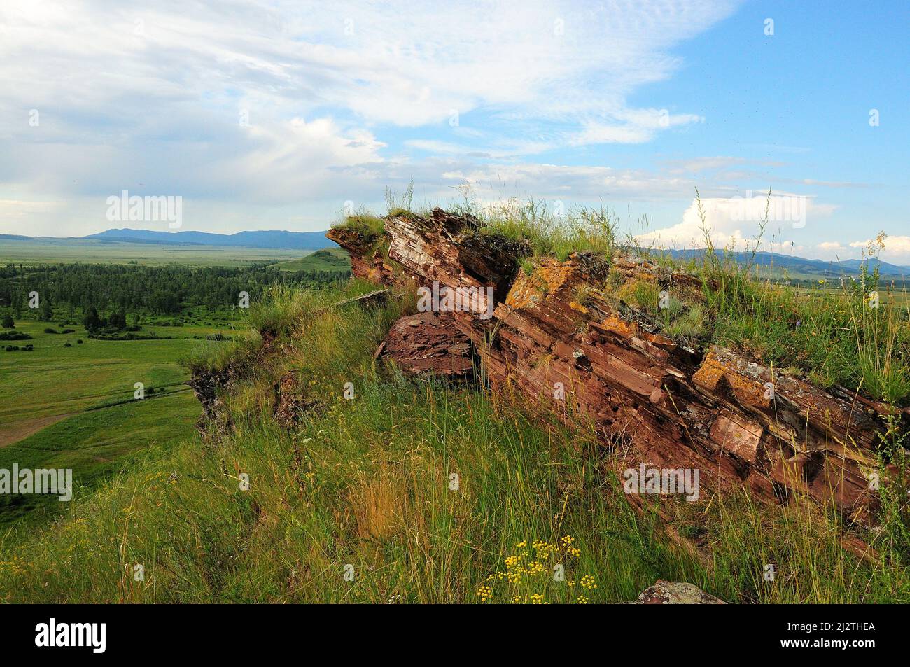 Formazioni di pietra arenaria stratificate sulla cima di un'alta collina che domina l'infinita steppa estiva. Catena montuosa Chests, Khakassia, Siberia, Russia. Foto Stock