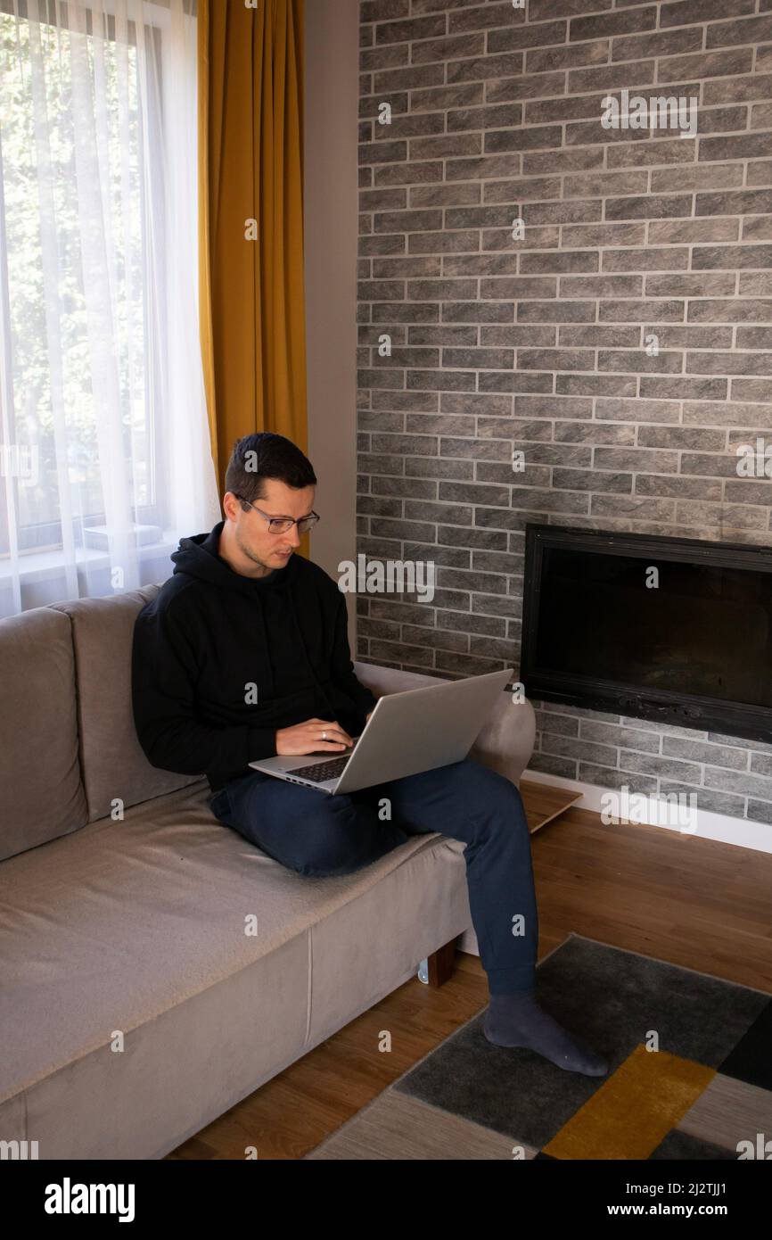 L'uomo con un computer portatile lavora da casa seduto sul divano Foto Stock