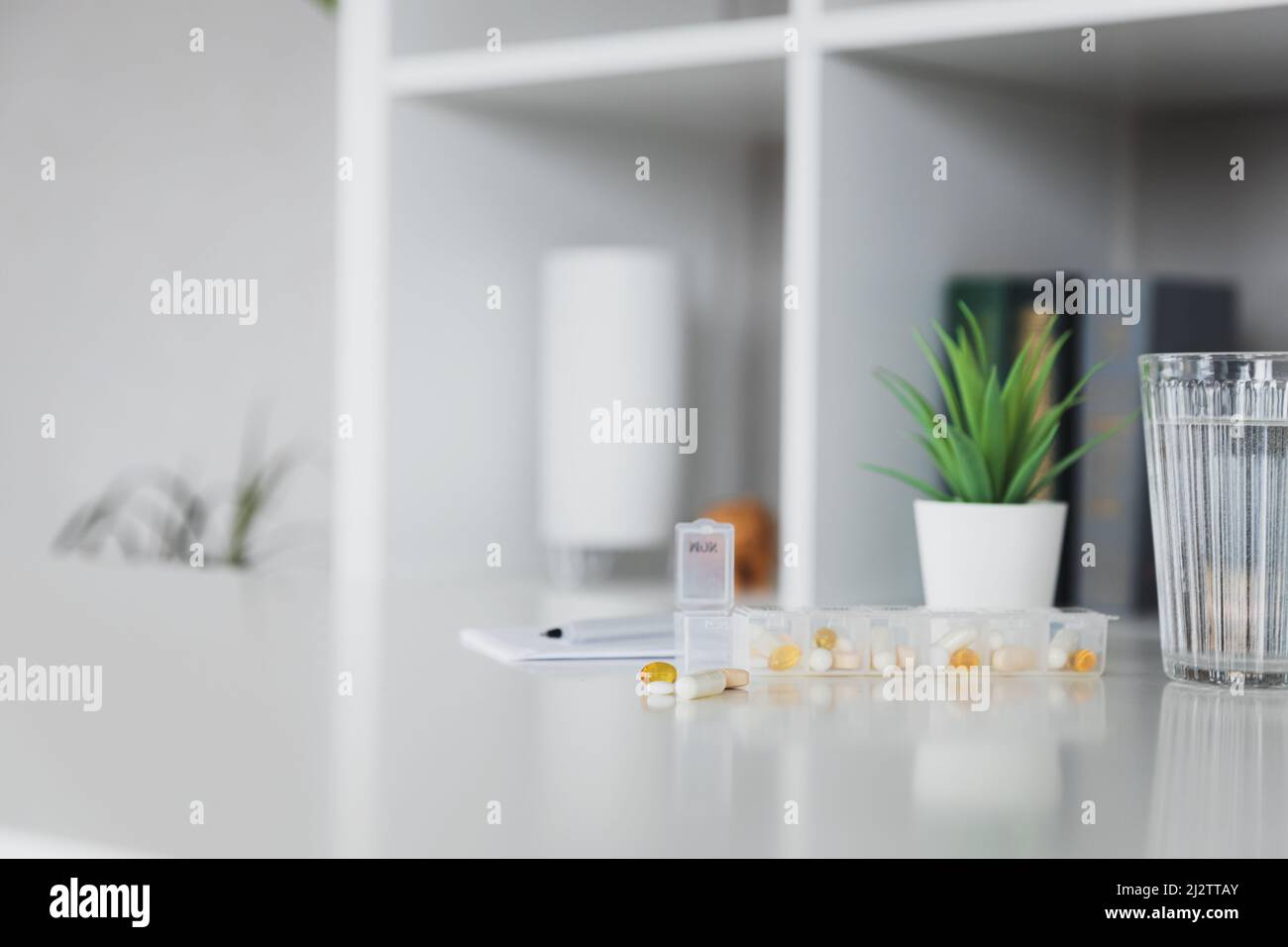 Primo piano della scatola della pillola medica sul tavolo con dosi di compresse per il giorno prendere un medicinale con farmaci bianchi, gialli e capsule usate per il trattamento, curare la malattia. Sfondo grigio degli scaffali, penna, blocco note Foto Stock