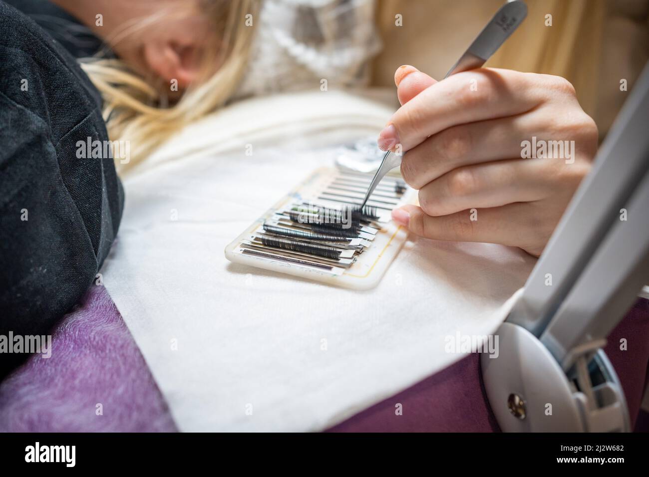 Il maestro prende un mazzo di ciglia artificiali curve con pinzette dalla tavoletta e si immerge nella colla. Il processo di estensione delle ciglia in un Foto Stock