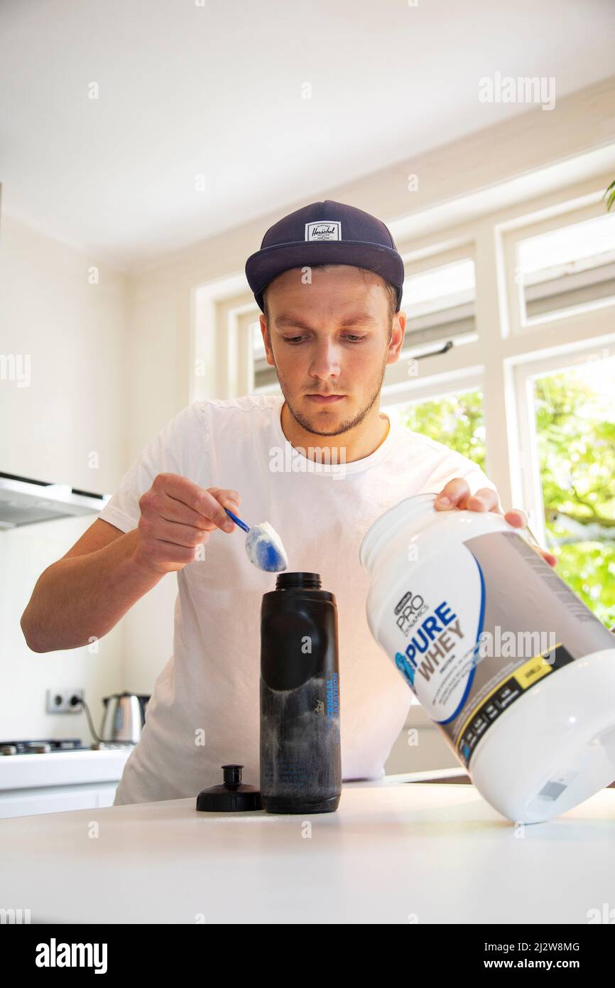 Shake proteico. Uomo sano sorridente con corpo muscolare preparazione bevanda sportiva prima di esercitarsi. Fitness maschio mettendo polvere con cucchiaio nel frullatore. B Foto Stock