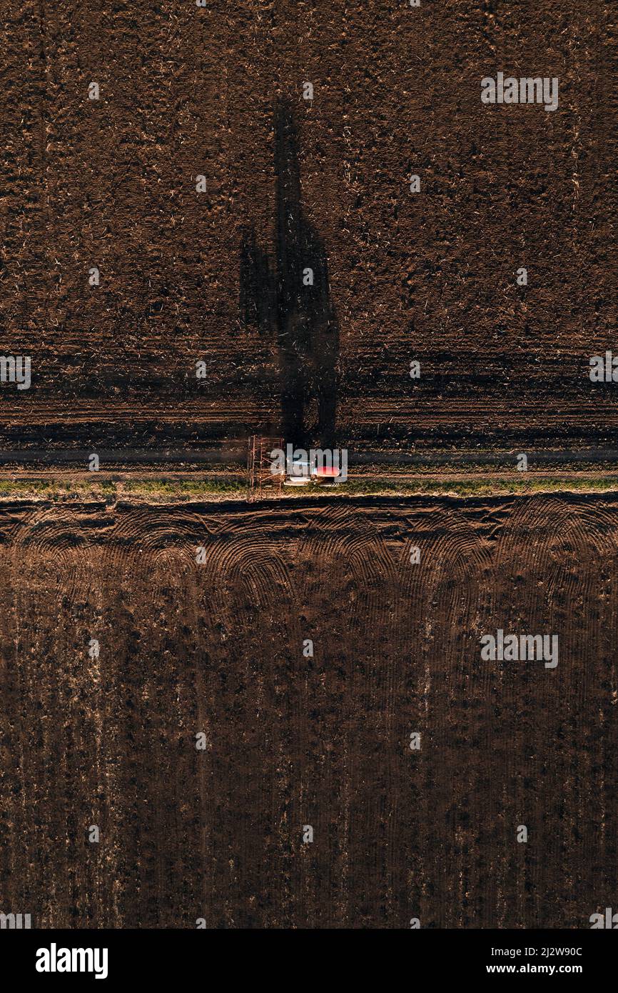 Vista aerea del trattore agricolo con timone collegato durante la guida su strada sterrata dopo il lavoro sul campo Foto Stock