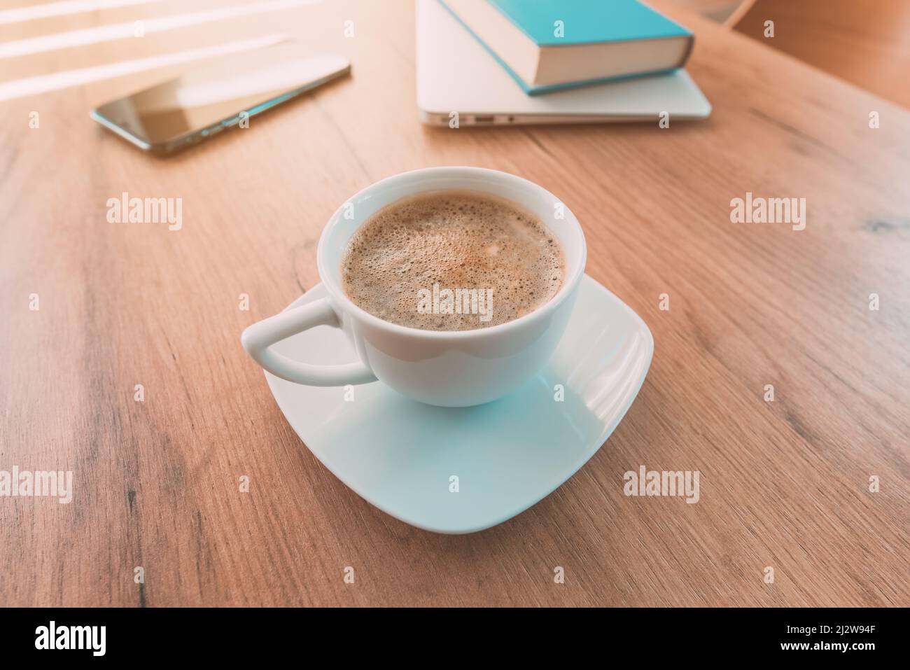 Importanza della caffeina e del caffè per il lavoro freelance. Tazza di caffè, smartphone mobile, computer portatile e un libro sul tavolo dell'ufficio domestico. Foto Stock