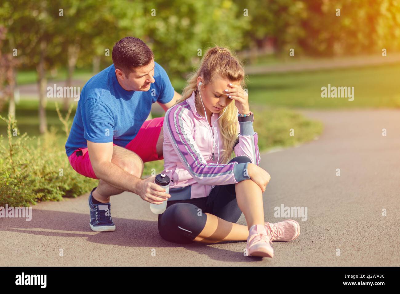 Giovane donna con lesioni al ginocchio mentre jogging all'aperto aiutata dal suo partner maschio Foto Stock