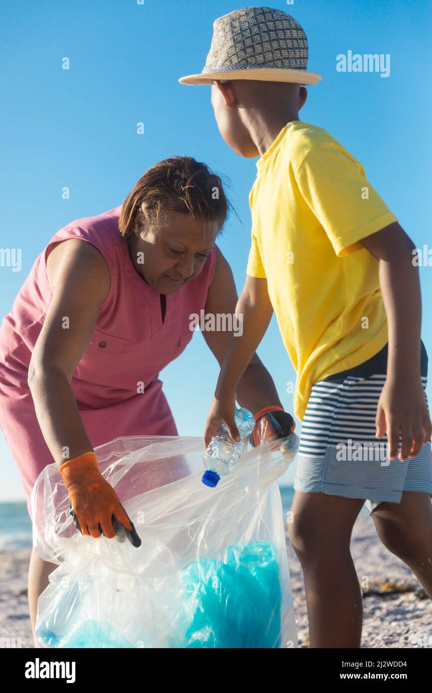 Nonna Africana americana che raccoglie rifiuti di plastica con il nipote in spiaggia il giorno di sole Foto Stock