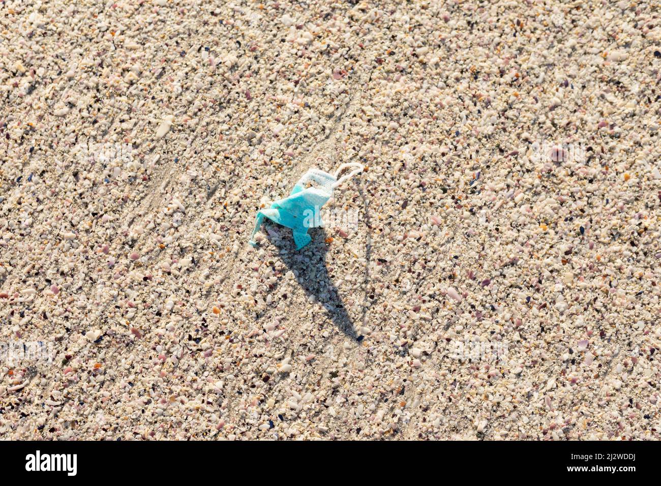 Direttamente sopra la vista della maschera protettiva abbandonata in sabbia bianca sulla spiaggia durante la giornata di sole Foto Stock