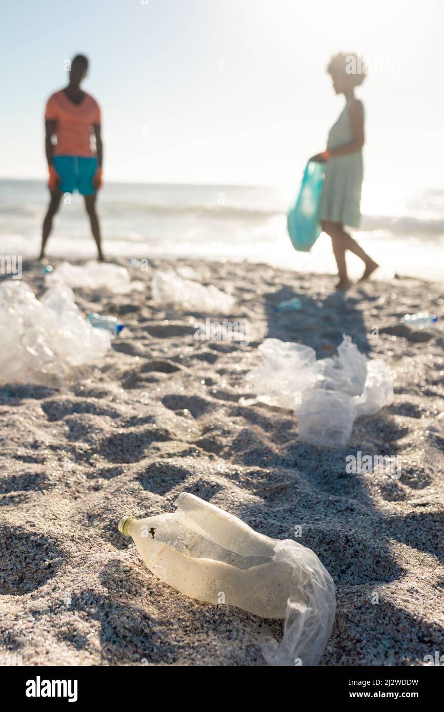 Vista a livello della superficie di rifiuti di plastica sparsi contro la spiaggia di pulizia coppia afro-americana Foto Stock