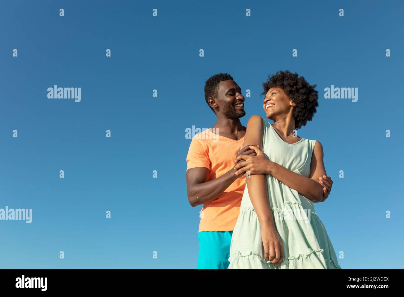 Vista ad angolo basso della coppia afroamericana sorridente contro il cielo blu chiaro con spazio copia Foto Stock