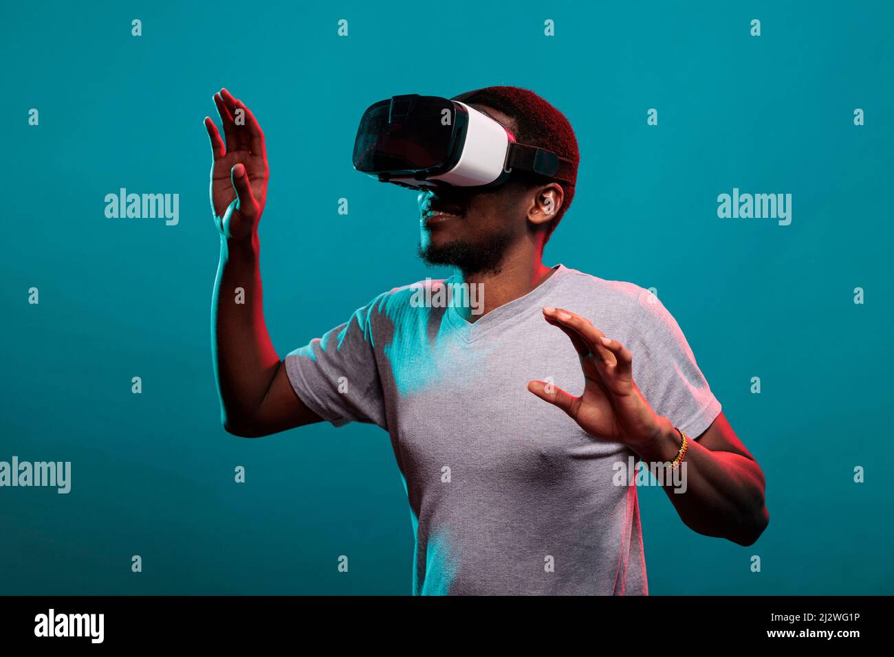 Uomo felice millenario che indossa occhiali vr con gioco futuristico e visione 3D, in piedi in studio. Giocare con occhiali per realtà virtuale e simulazione visiva interattiva, tecnologia moderna. Foto Stock
