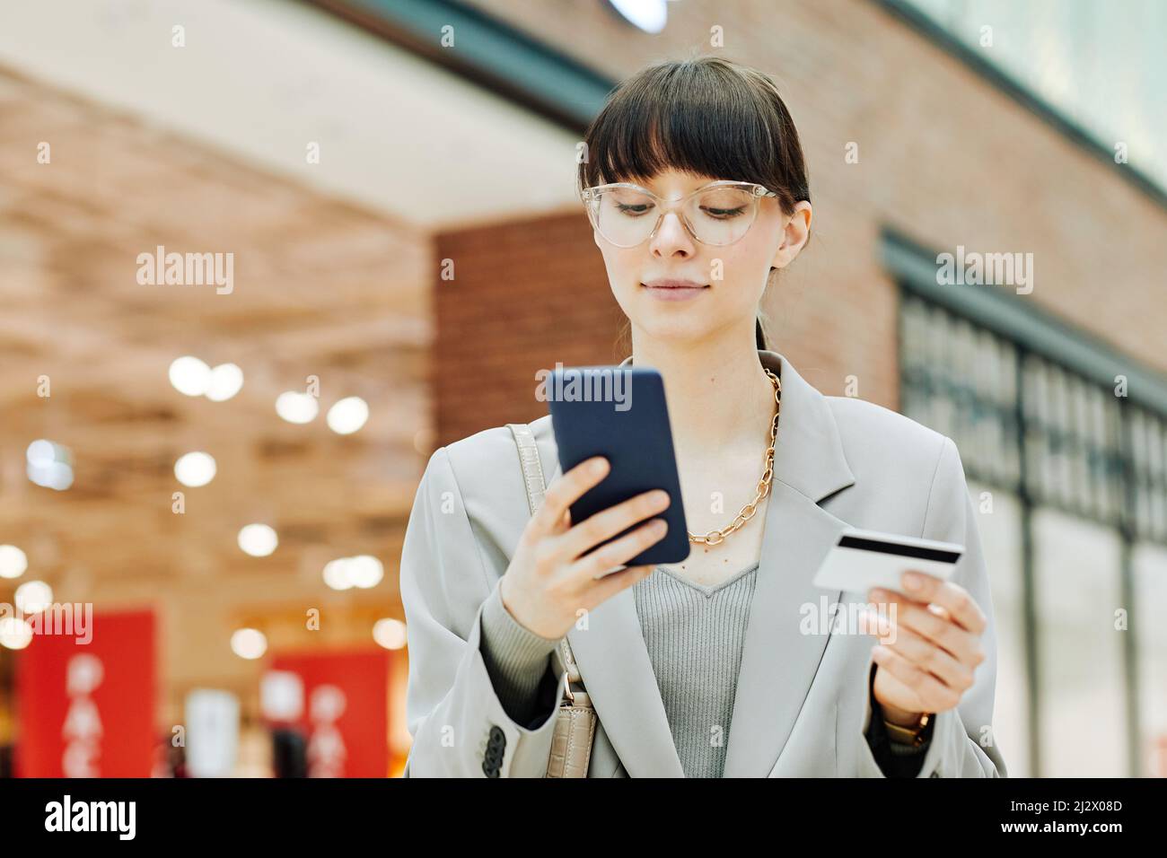 Ritratto della giovane donna che inserisce le informazioni della carta di credito online nello smartphone mentre si trova all'interno del centro commerciale, spazio copia Foto Stock
