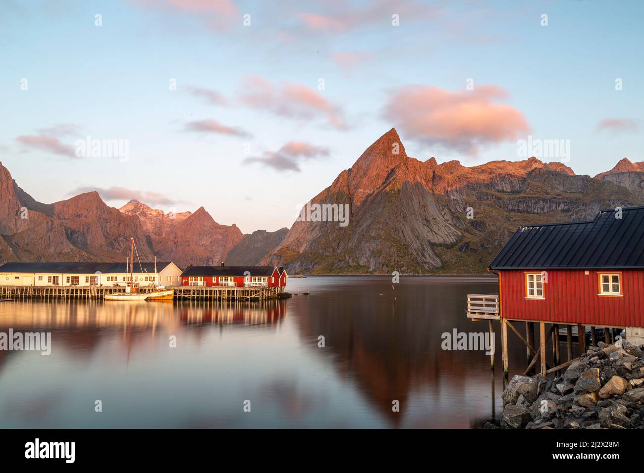 Barche da pesca, case rosse nel porto di Hamnoy, Moskenesoy, Lofoten, Norvegia. Luce del sole sulle cime di montagna. Foto Stock