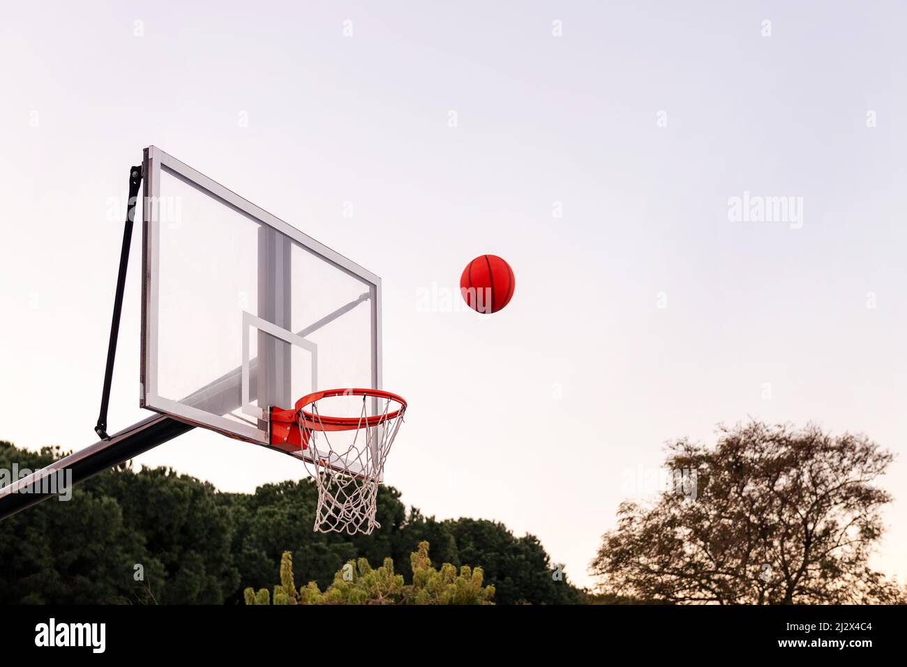 pallina che vola su un cerchio di basket con il cielo sullo sfondo, concetto di sport urbano all'aperto, spazio di copia per il testo Foto Stock
