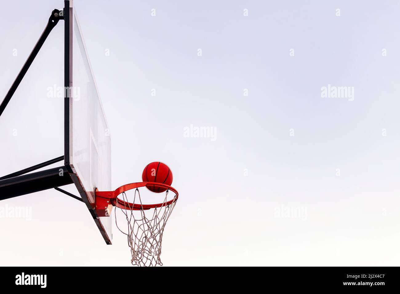 palla che entra in un cerchio di basket con il cielo sullo sfondo, concetto di sport urbano all'aperto, copia spazio per il testo Foto Stock