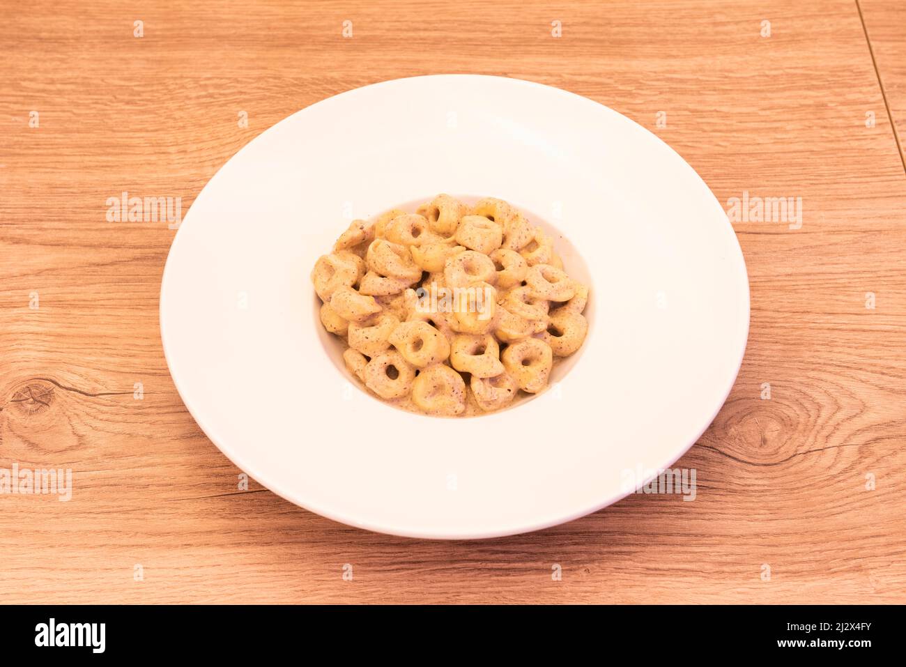 Piatto di deliziosi tortellini in salsa di tartufo su piatto bianco e tavola di legno chiaro con nodi Foto Stock