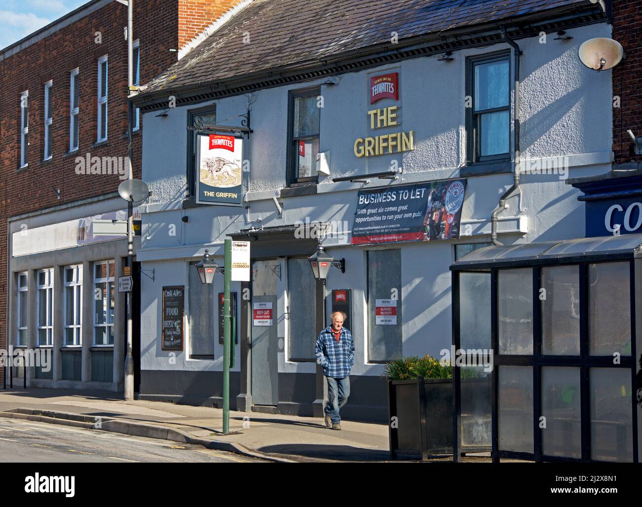Uomo che cammina accanto al pub Griffin - chiuso e chiuso - su High Street, Market Weighton, East Yorkshire, Inghilterra Regno Unito Foto Stock