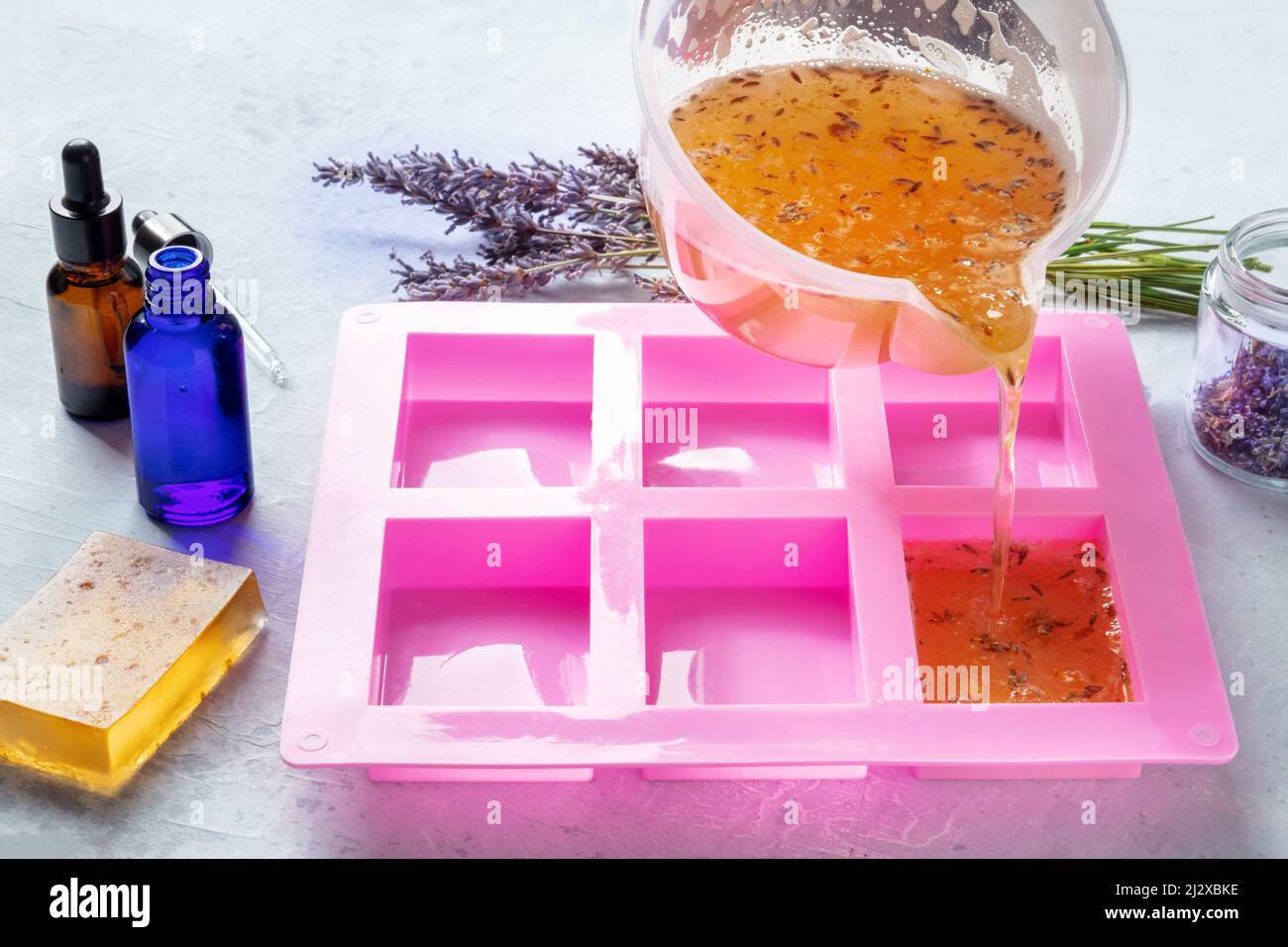 Sapone organico fatto a mano, il processo di fabbricazione. Glicerina liquida con fiori di lavanda e oli essenziali versati in uno stampo per formarsi successivamente in barre Foto Stock