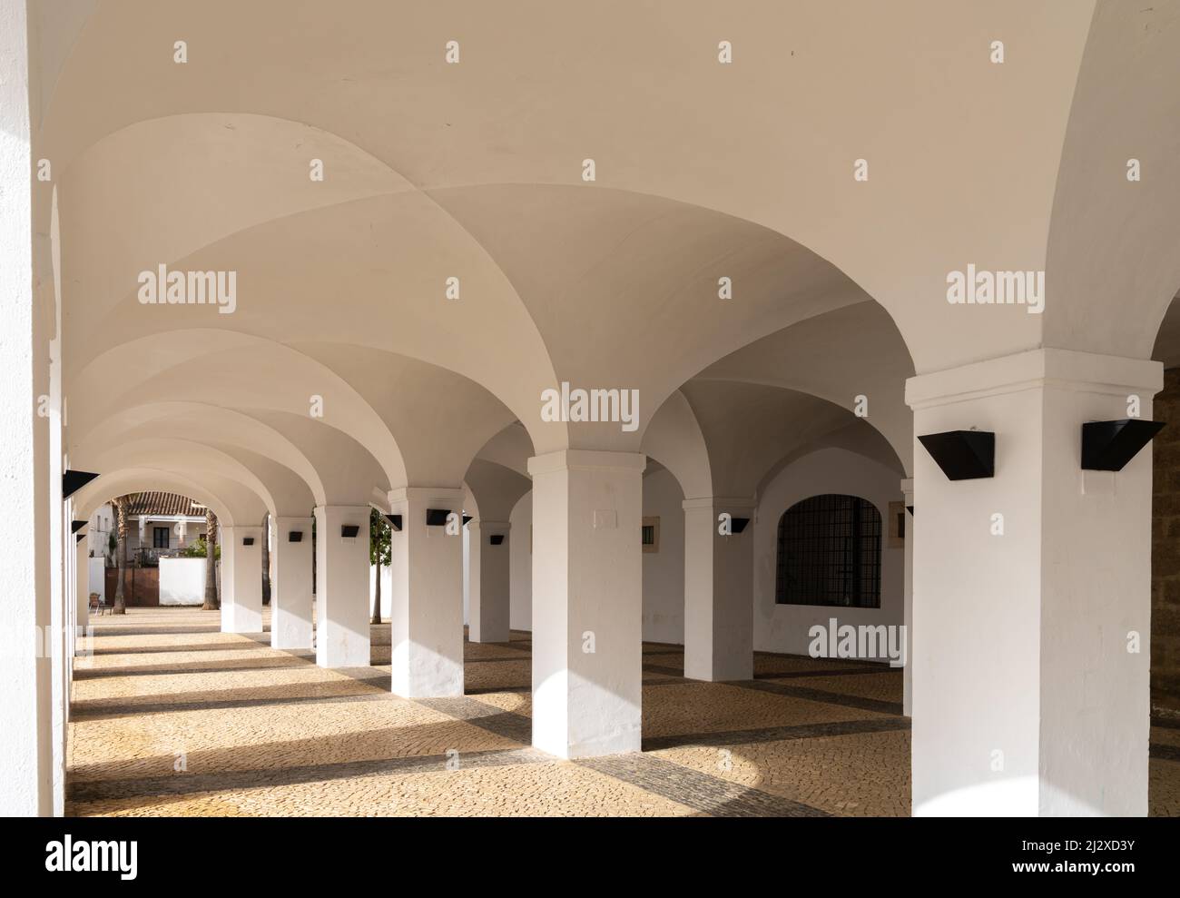Olivenza, Spagna - 27 marzo 2022: Portico dipinto di bianco con molti archi e pavimento in pietra a motivi geometrici Foto Stock