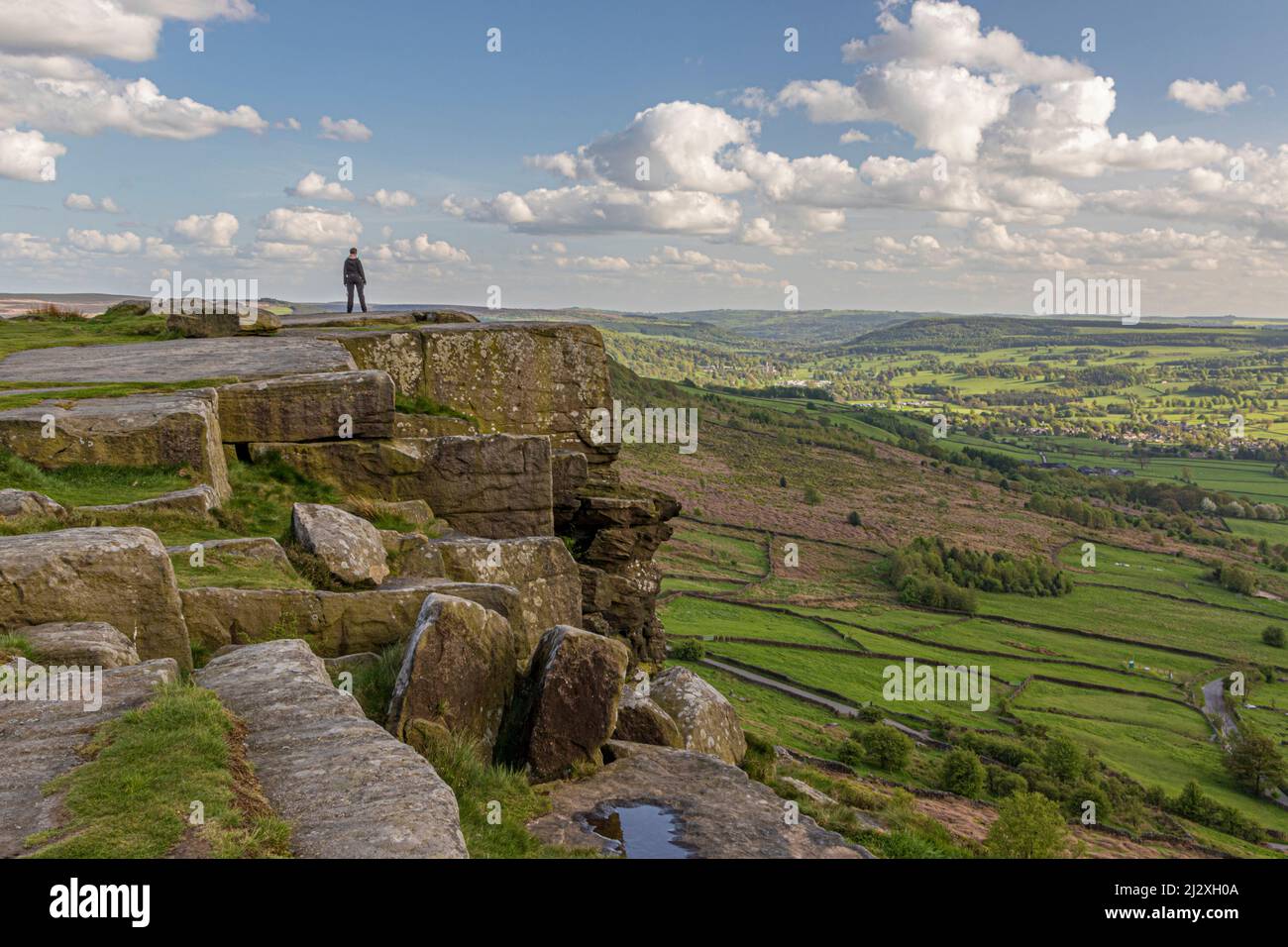 Persona in piedi sul bordo della scogliera che guarda verso la valle a Curbar Edge, Peak District, Inghilterra, Regno Unito Foto Stock
