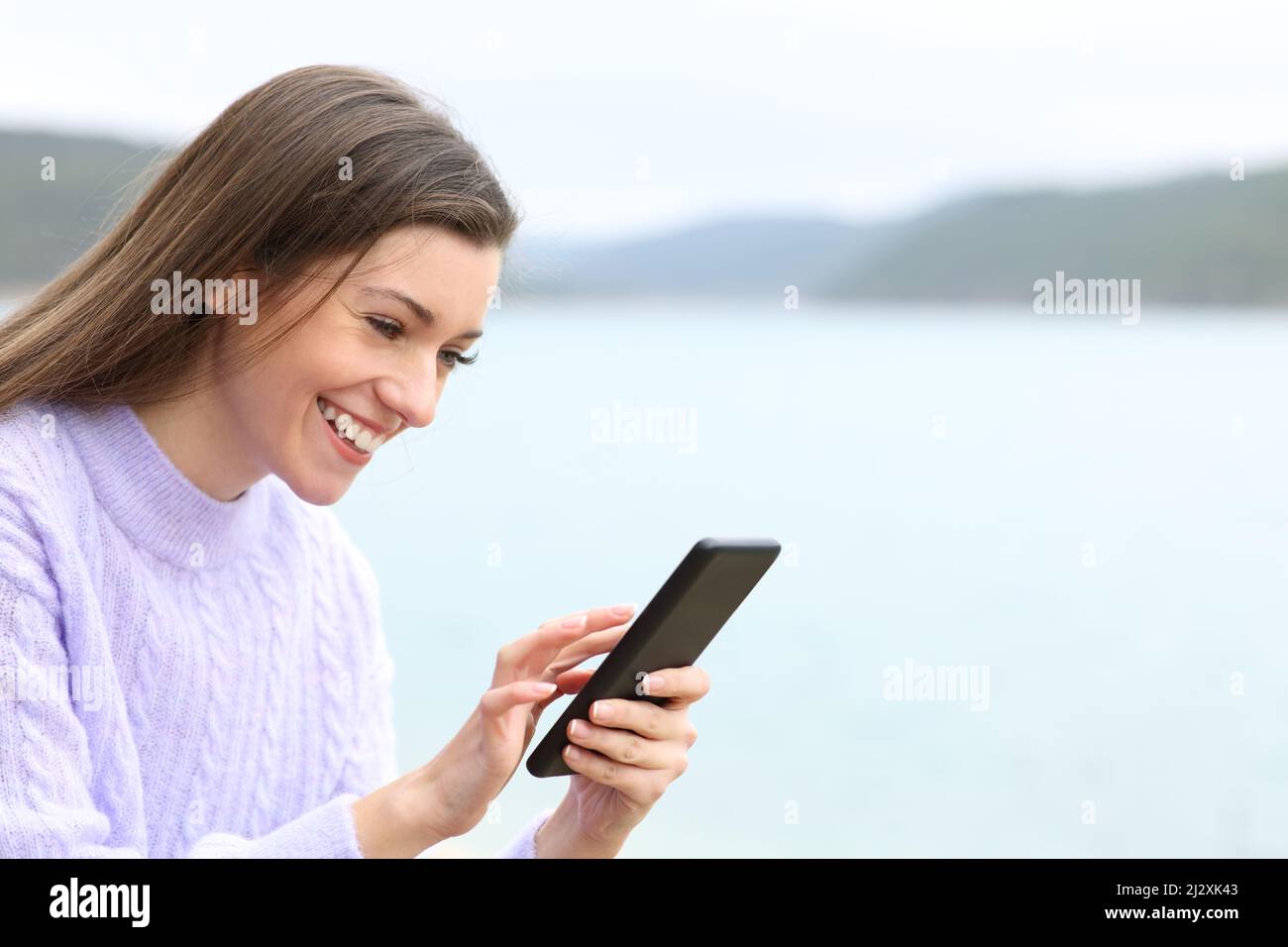 Buon adolescente che controlla il contenuto del telefono cellulare seduto in un lago Foto Stock
