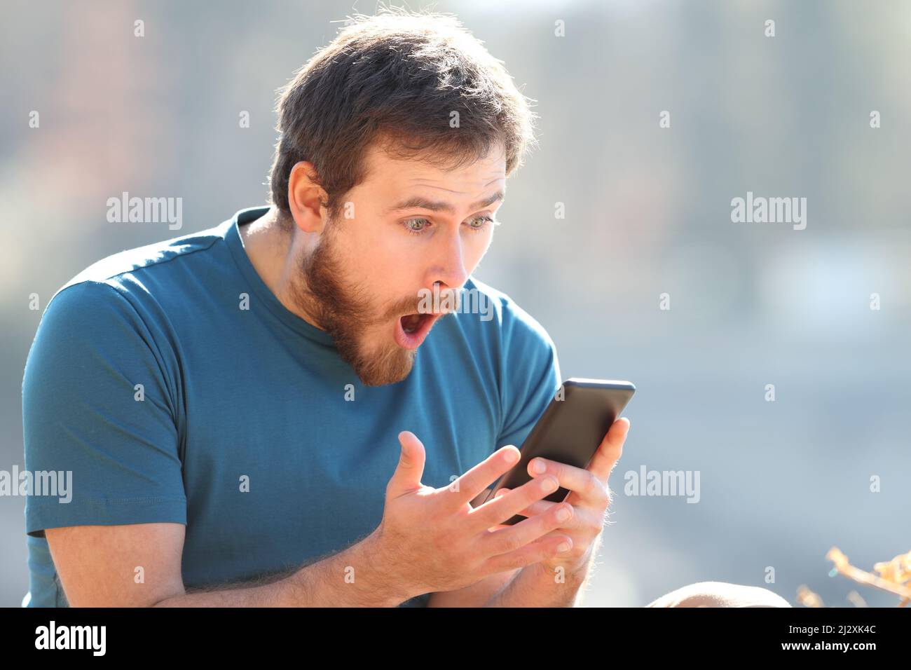 Stupito uomo che controlla i contenuti del telefono cellulare all'aperto Foto Stock