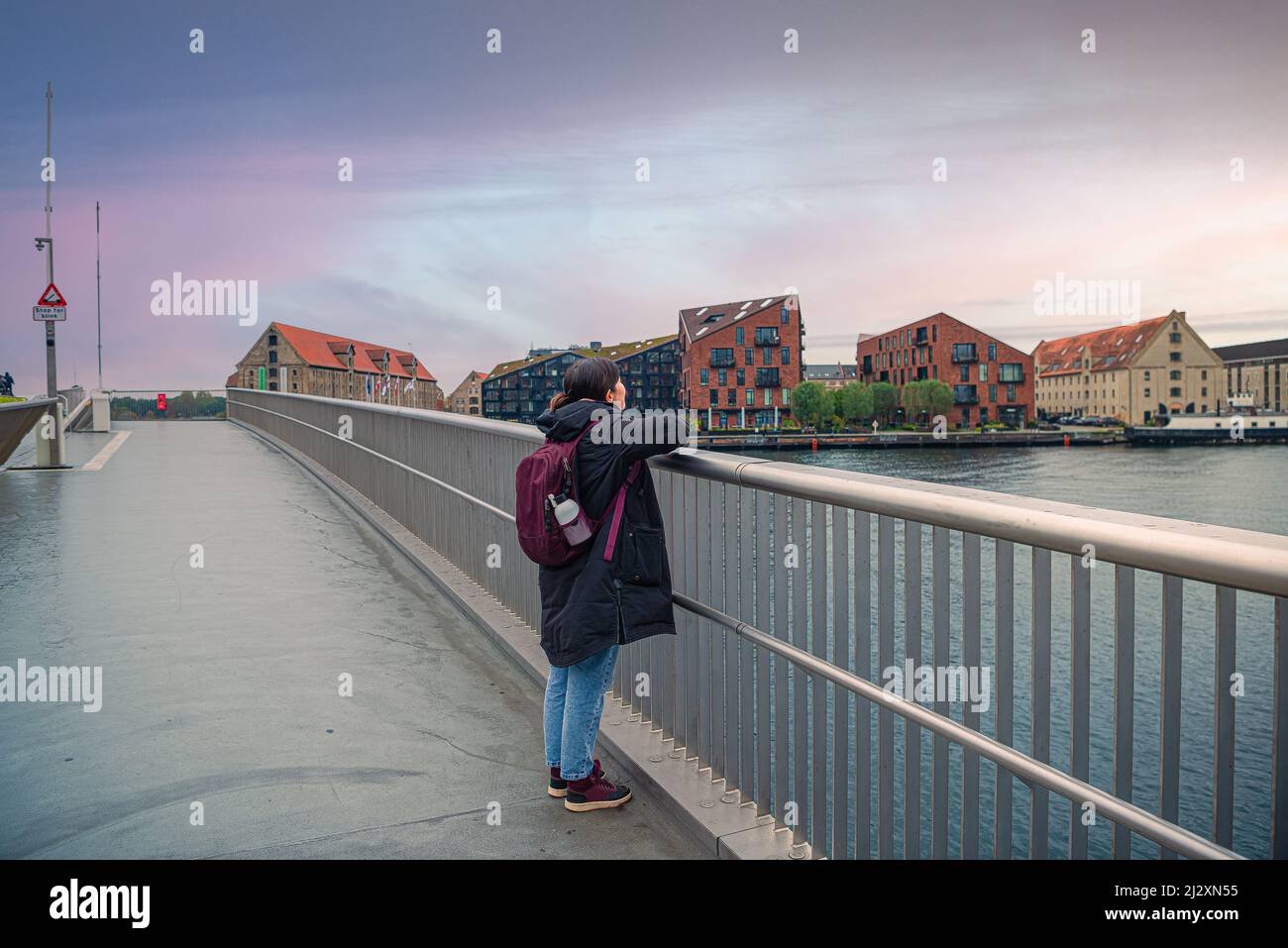 Brunette ragazza in abiti caldi guarda appoggiati su corrimano interno Porto pedonale e ponte bicyclist Inderhavnsbroen contro il quartiere Chris Foto Stock