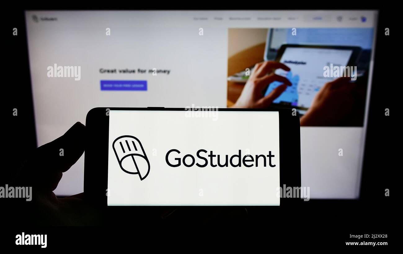 Persona che tiene uno smartphone con il logo della società di tutoring austriaca GoStudent GmbH sullo schermo di fronte al sito web. Mettere a fuoco sul display del telefono. Foto Stock