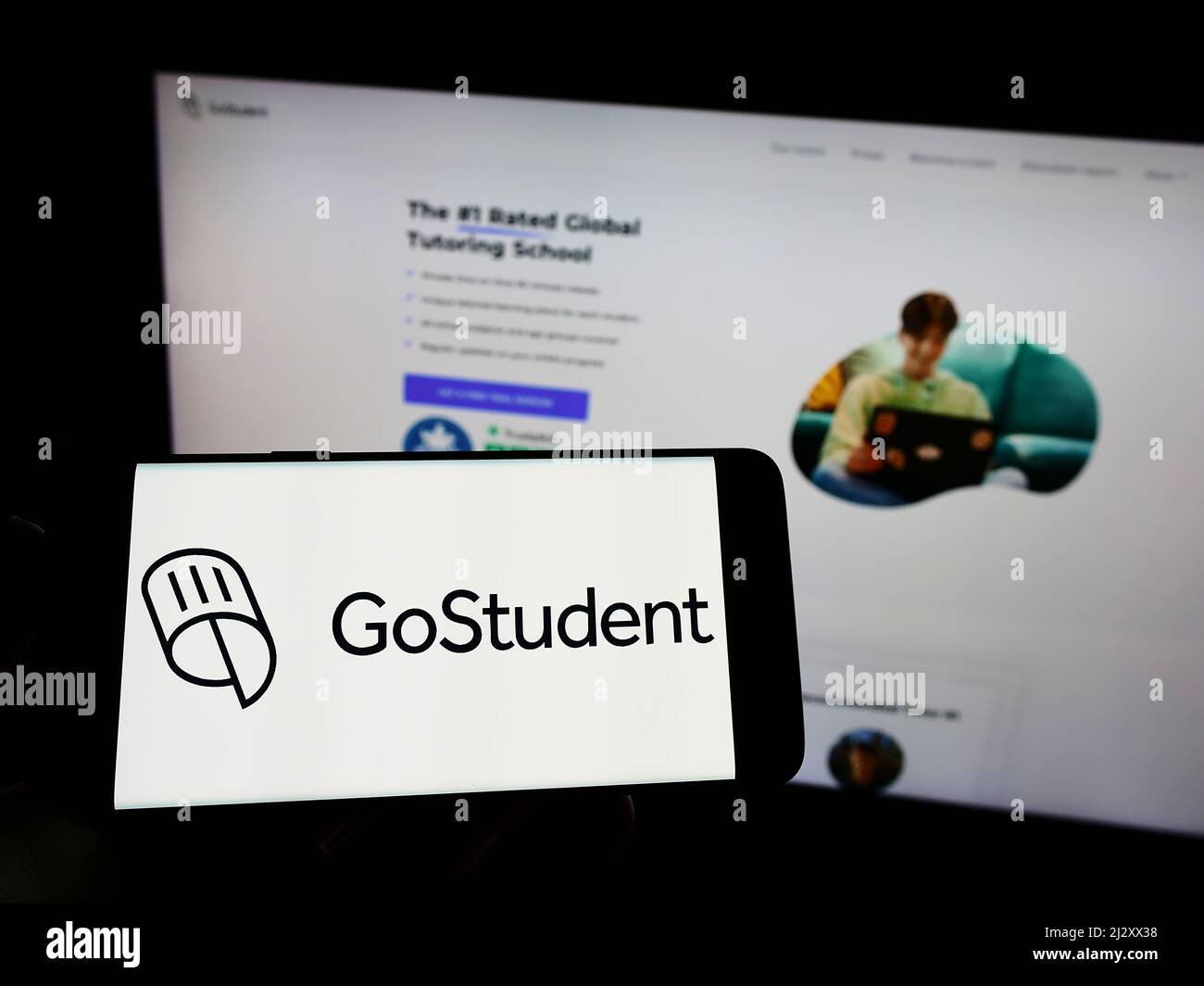 Persona che tiene il cellulare con il logo della società di tutoring austriaca GoStudent GmbH sullo schermo di fronte al sito web aziendale. Mettere a fuoco sul display del telefono. Foto Stock