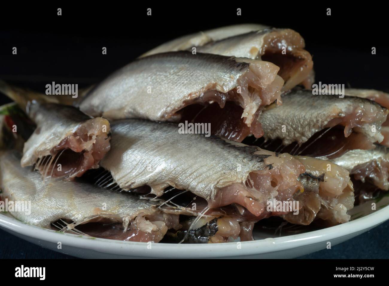 Pesce salato in un piatto bianco sul tavolo. Cibo su sfondo nero Foto Stock