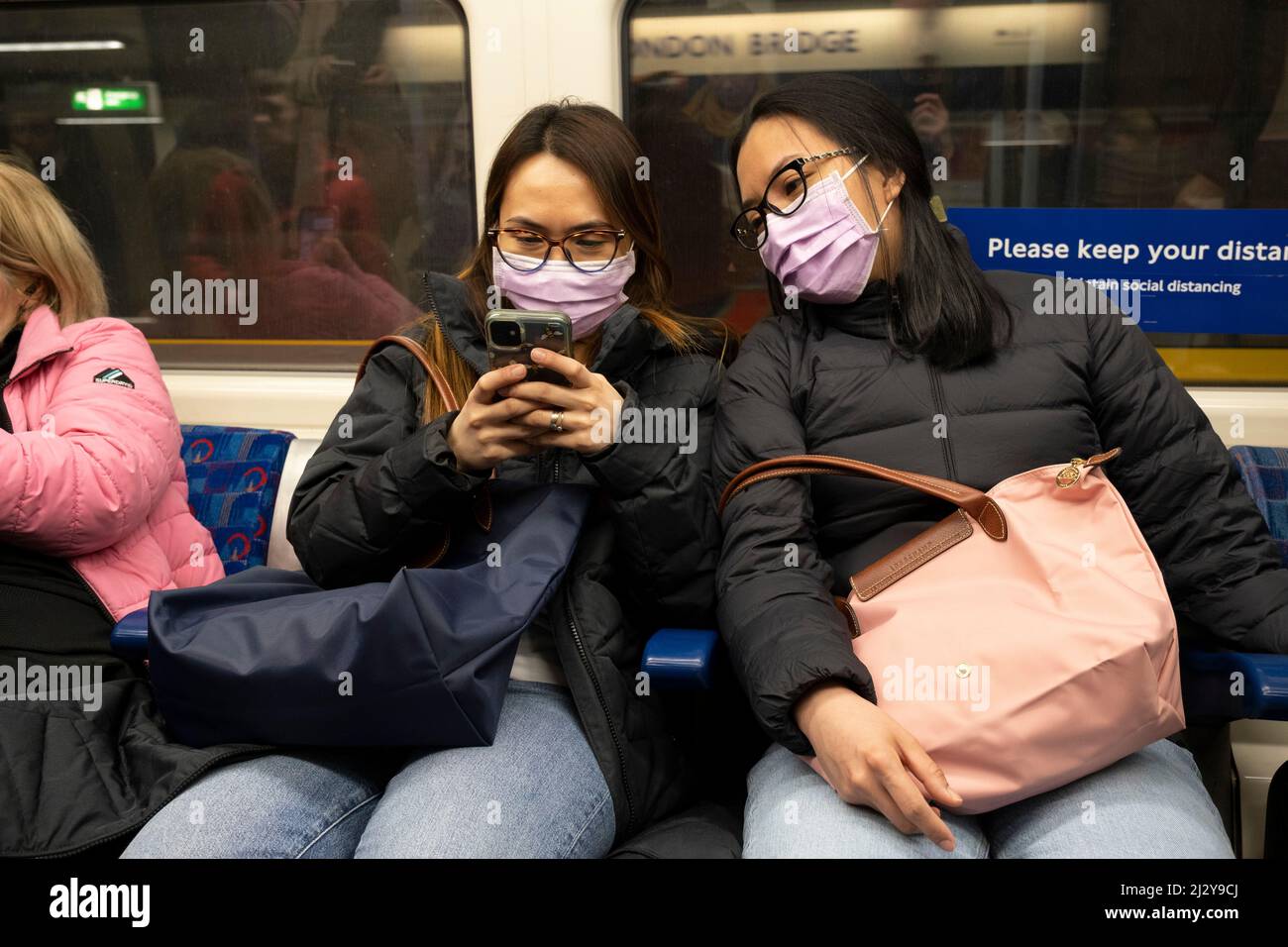 Due donne che indossano maschere facciali su un treno della metropolitana di Londra il 17th marzo 2022 a Londra, Regno Unito. Mentre l'uso obbligatorio di rivestimenti per il viso nei luoghi pubblici è terminato, i consigli di copertura del viso da parte di TfL Transport per Londra in questo momento sono i seguenti: È necessario indossare una copertura per il viso, sopra il naso e la bocca, sulla rete di trasporto per Londra, nelle stazioni, e per l'intero viaggio. In caso contrario, e non sei esente, potresti essere rifiutato di entrare, di viaggiare o di lasciare le nostre stazioni e servizi. Foto Stock