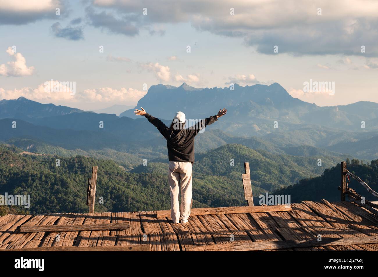 Allegra vista posteriore di donna asiatica in piedi braccia sollevate su balcone di legno con cima di montagna nella campagna a Chiang mai, Thailandia Foto Stock