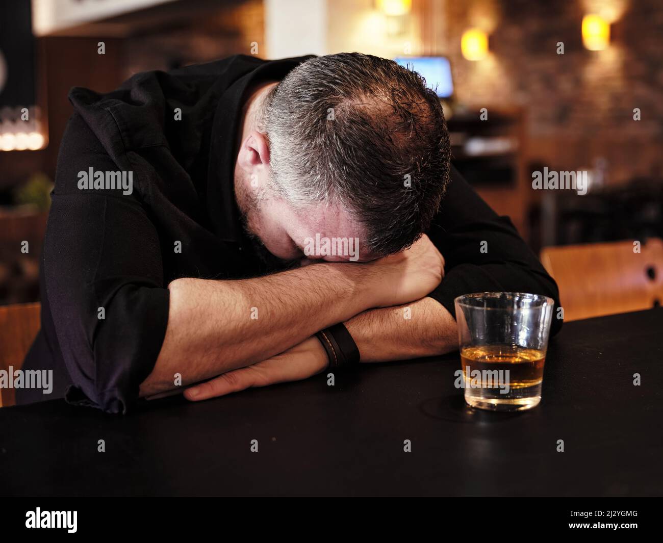 Il cliente ubriaco di sesso maschile dorme sul banco del bar con un bicchiere di whiskey al pub. Dipendenza da alcol, problema di bere. Foto Stock