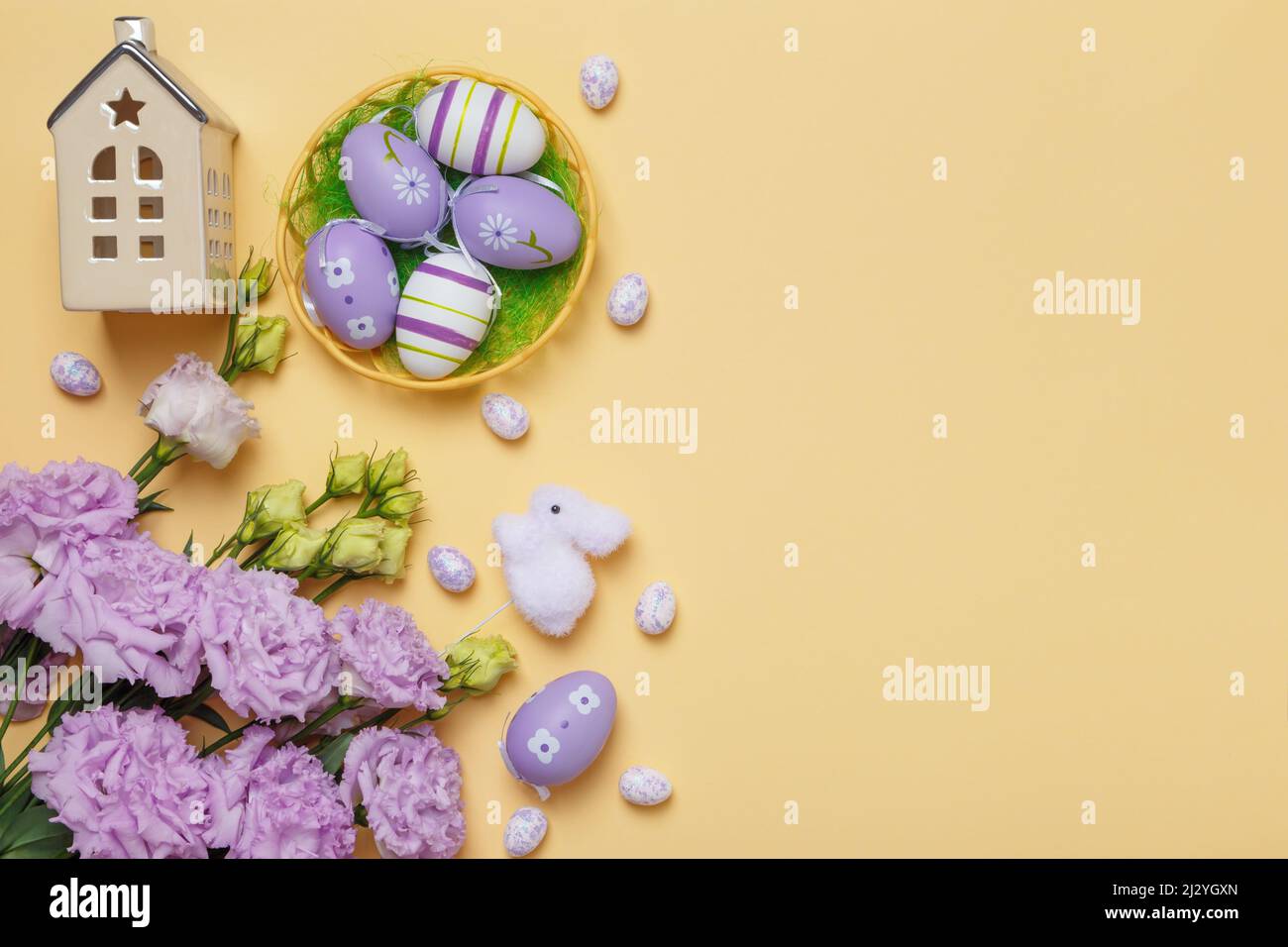 Carta di Pasqua. Piccolo giocattolo casa uova in un bouquet cestino di fiori viola su uno sfondo giallo con spazio copia. Foto Stock